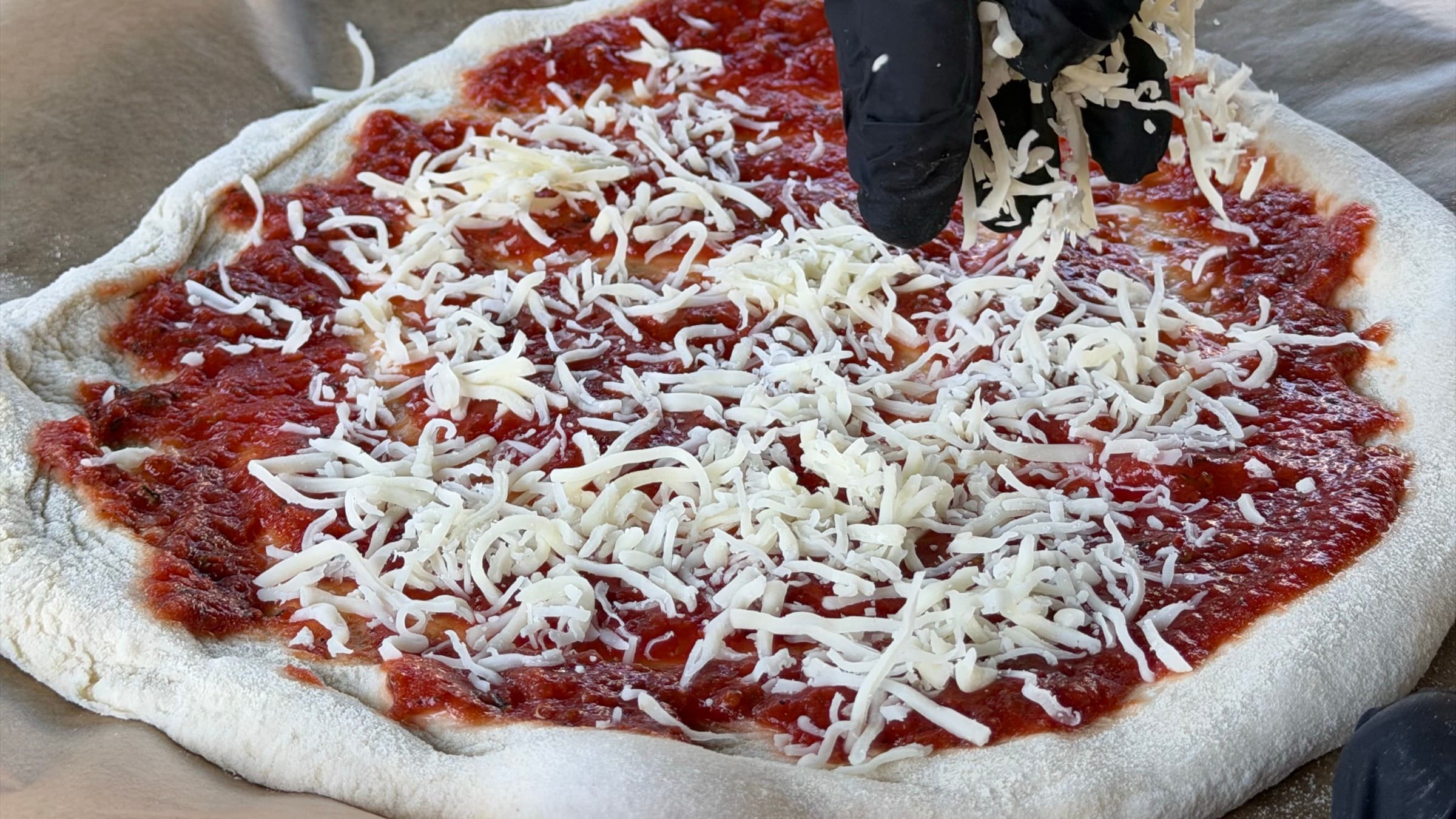 Pizzateig mit Tomatensauce wird vor dem Backen mit Käse belegt