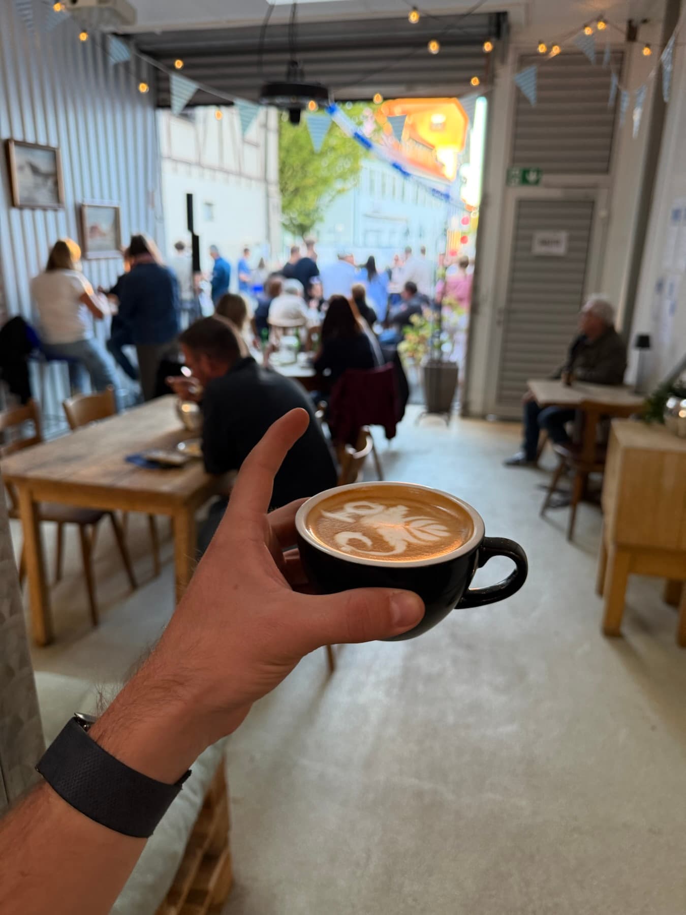 Cappuccino in der Hand, im Hintergrund Gäste beim Pop-up-Café
