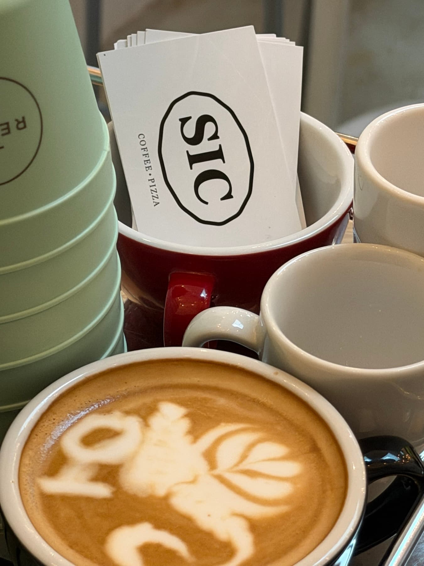 Cappuccino mit Latte Art vor SIC Coffee Pizza Visitenkarten